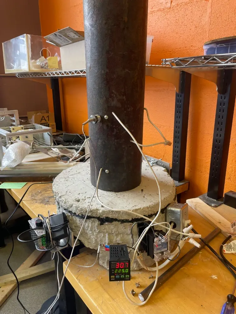 Capstone pyrolysis reactor — steel cylinder mounted on a hand-poured concrete base in the lab